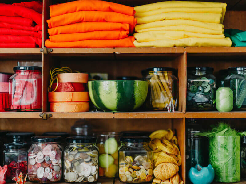 Shelving unit filled with colour-coordinated craft supplies such as buttons, fabric and ribbon